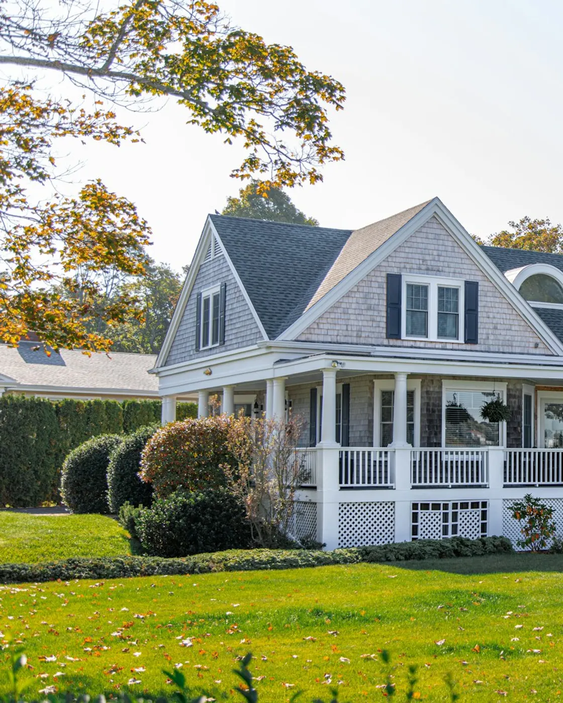 A classic American home with a wraparound porch on a green lawn in warm autumn light